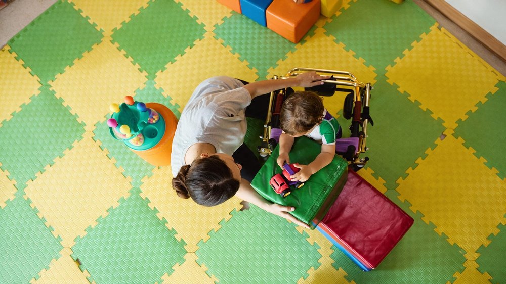 A specialist playing with a child on a colorful play mat in the center